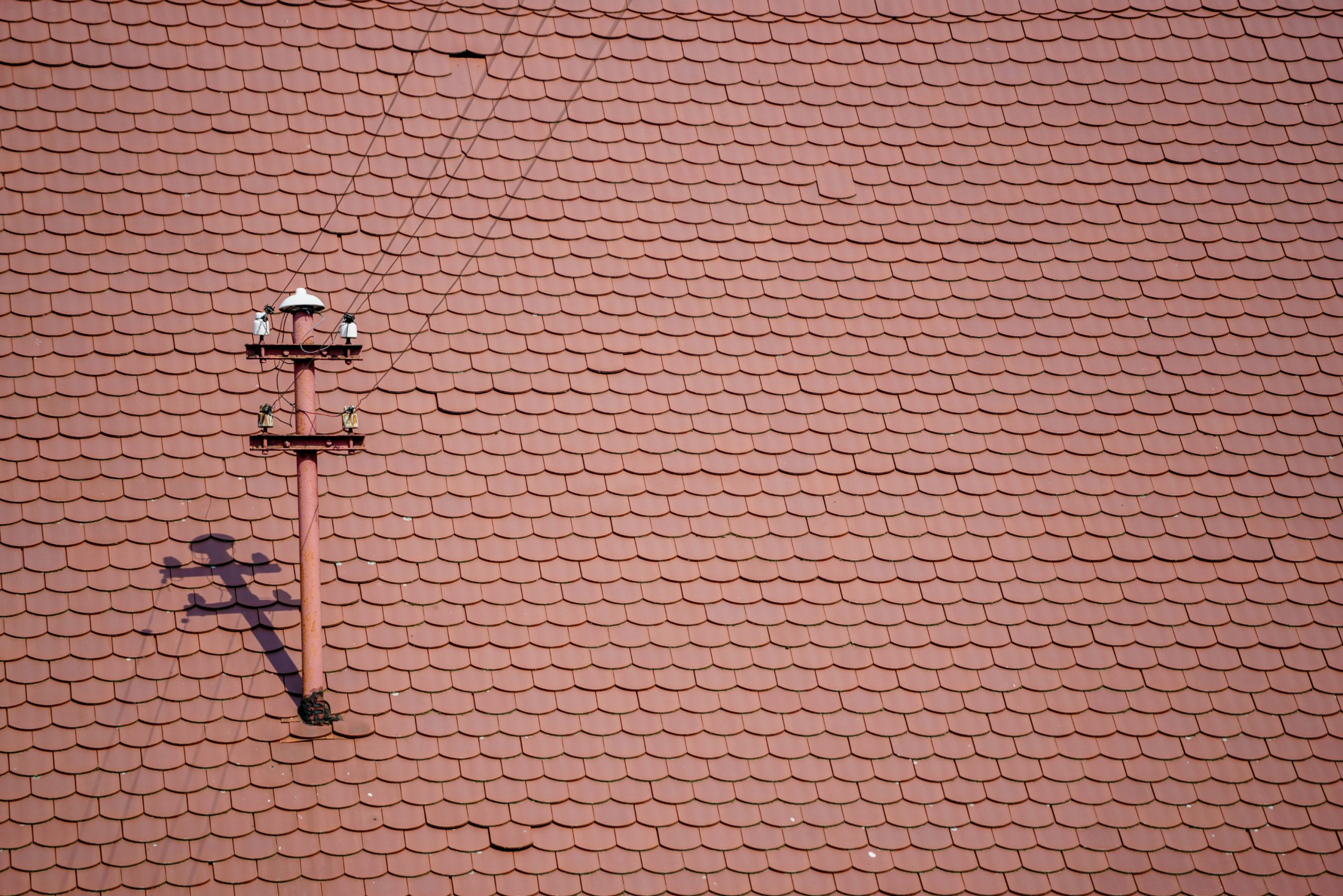 Reddish tiled roof with a utility pole and cables casting a detailed shadow. Bright lighting emphasizes the pattern and texture.