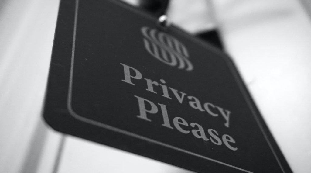 Black and white close-up of a "Privacy Please" door hanger with a logo, conveying a mood of calm and privacy.