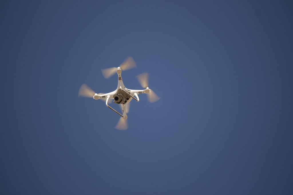 A white drone with spinning propellers flies against a clear blue sky, capturing a serene and open-air atmosphere.