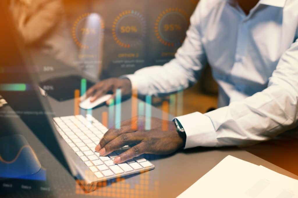 A person in a white shirt types on a keyboard at a desk. Transparent graphs and charts overlay the image, conveying a data-driven, professional atmosphere.