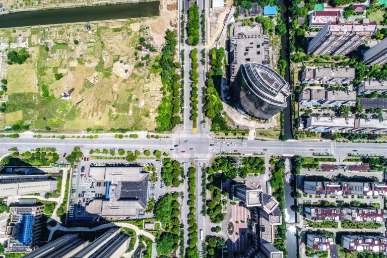 Aerial view of an urban area with a grid of streets intersecting. Surrounding tall buildings, green parks, and a river convey a busy, organized cityscape.