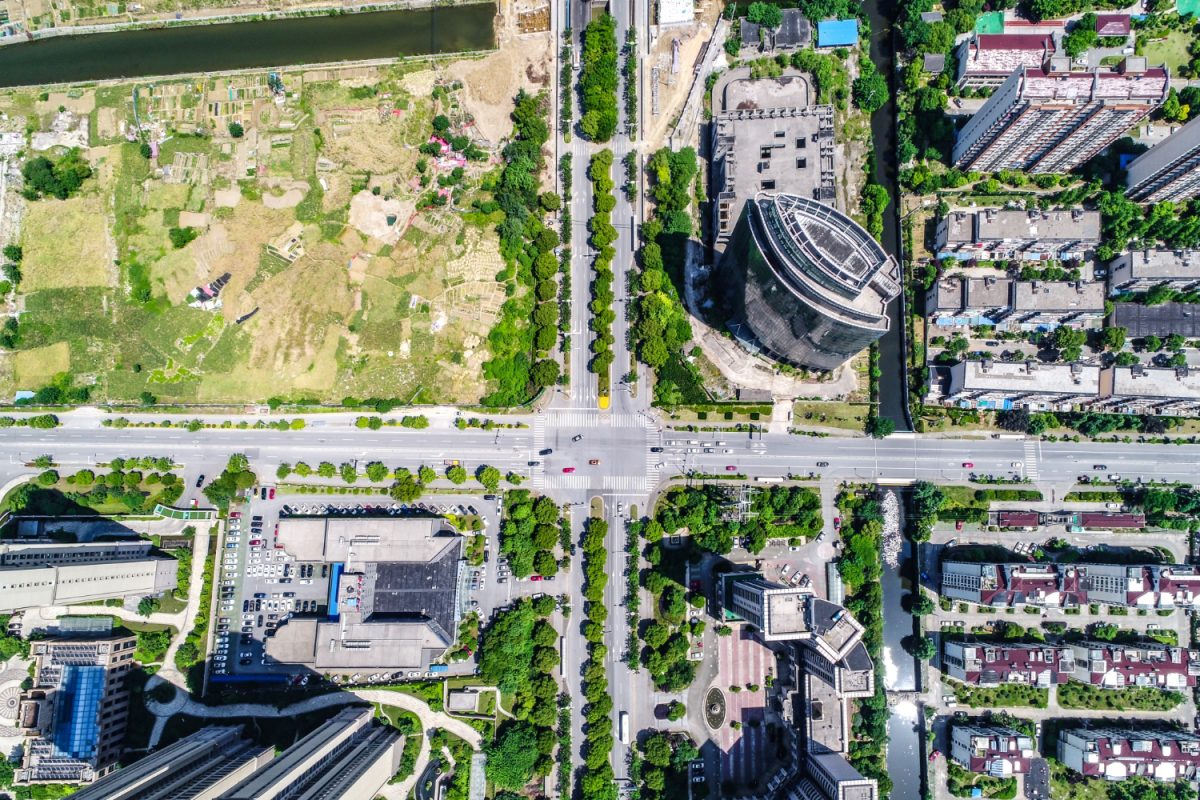Aerial view of an urban area with a grid of streets intersecting. Surrounding tall buildings, green parks, and a river convey a busy, organized cityscape.