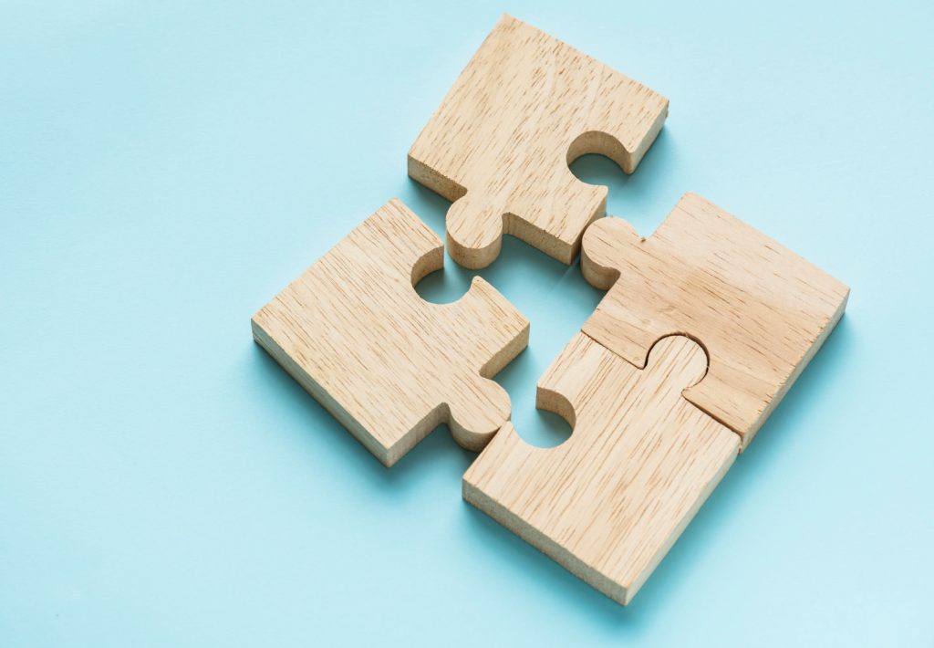 Wooden puzzle pieces interlocked on a light blue background, symbolizing connection and teamwork. The minimalist design conveys simplicity and unity.