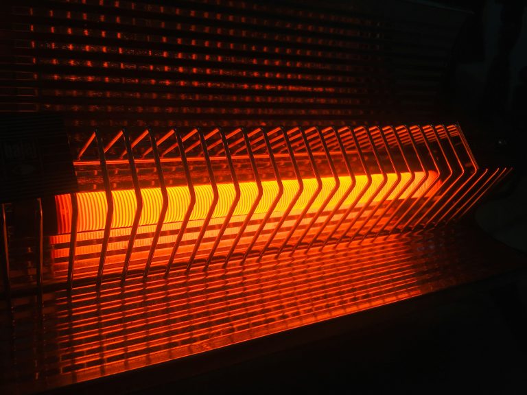 Orange-red electric heater with a metal grill glows brightly, casting warm light and shadows. The tone is cozy and inviting, emphasizing warmth.