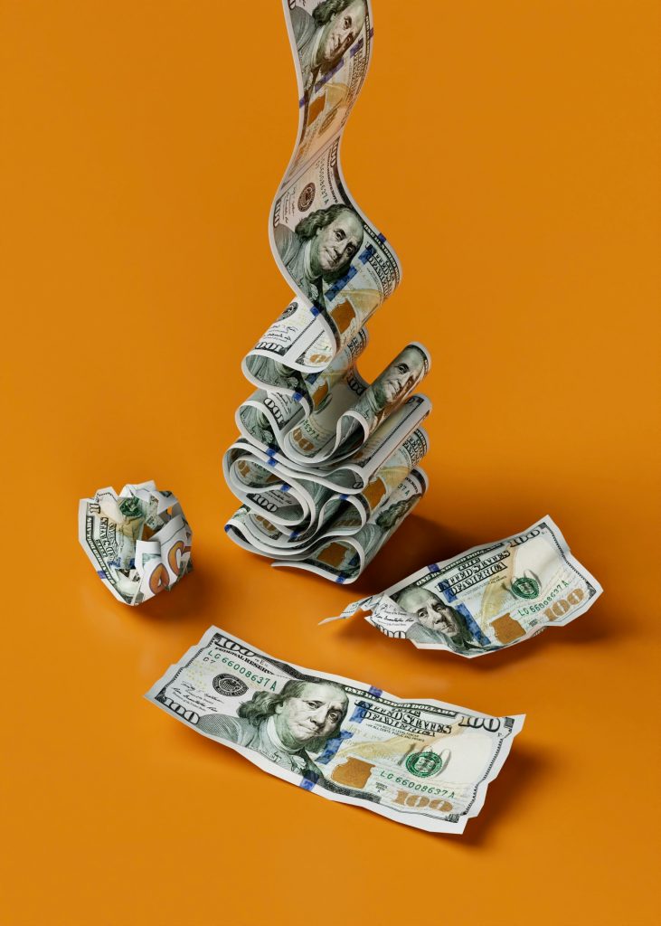 Crumpled, rolled, and straight hundred-dollar bills on an orange background, creatively arranged to form an abstract art piece.